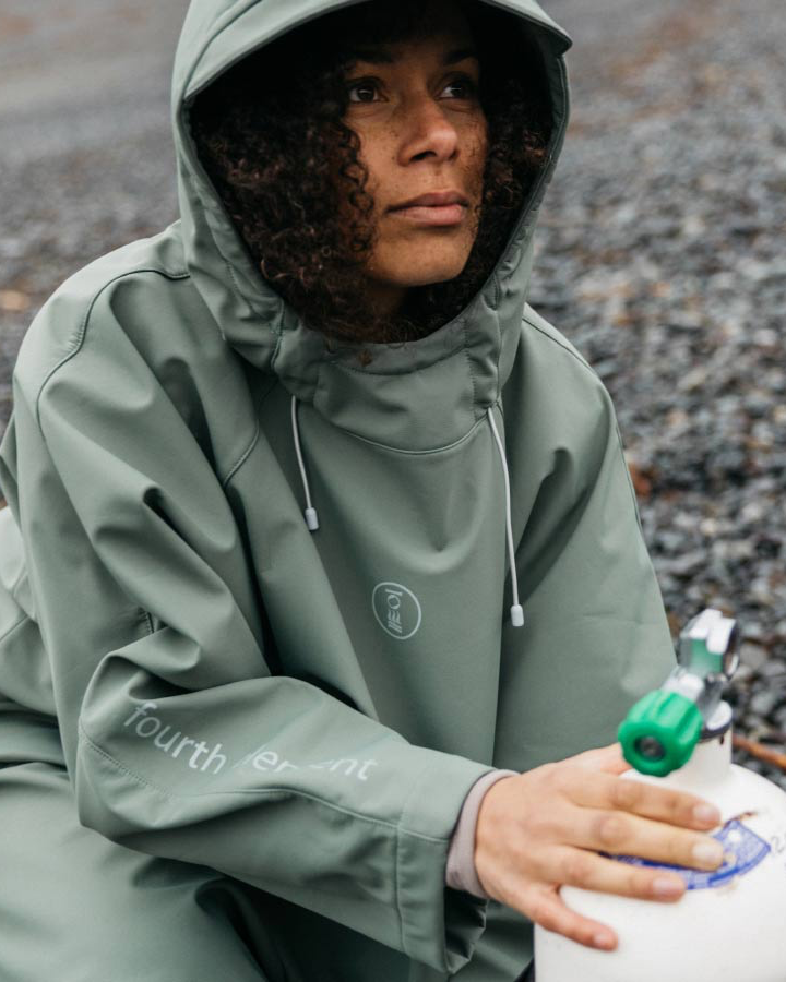 Person wearing a green raincoat holding a white container with a green lid on a gravel surface.