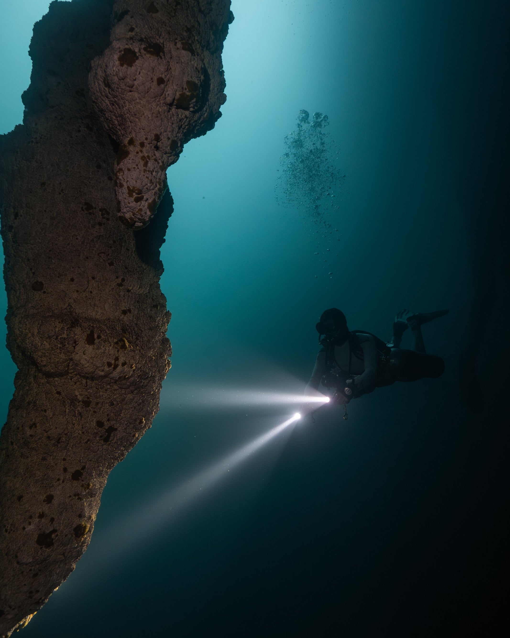 Diver exploring a dark underwater cave with a flashlight.