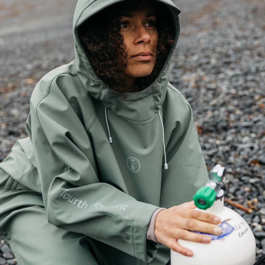 Person wearing a green raincoat holding a white container with a green lid on a gravel surface.